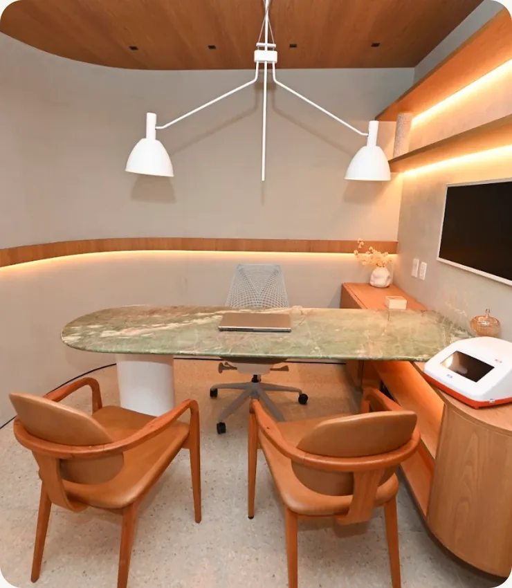 Consultório amplo do INME com mesa oval de mármore verde, luminárias pendentes e poltronas caramelo