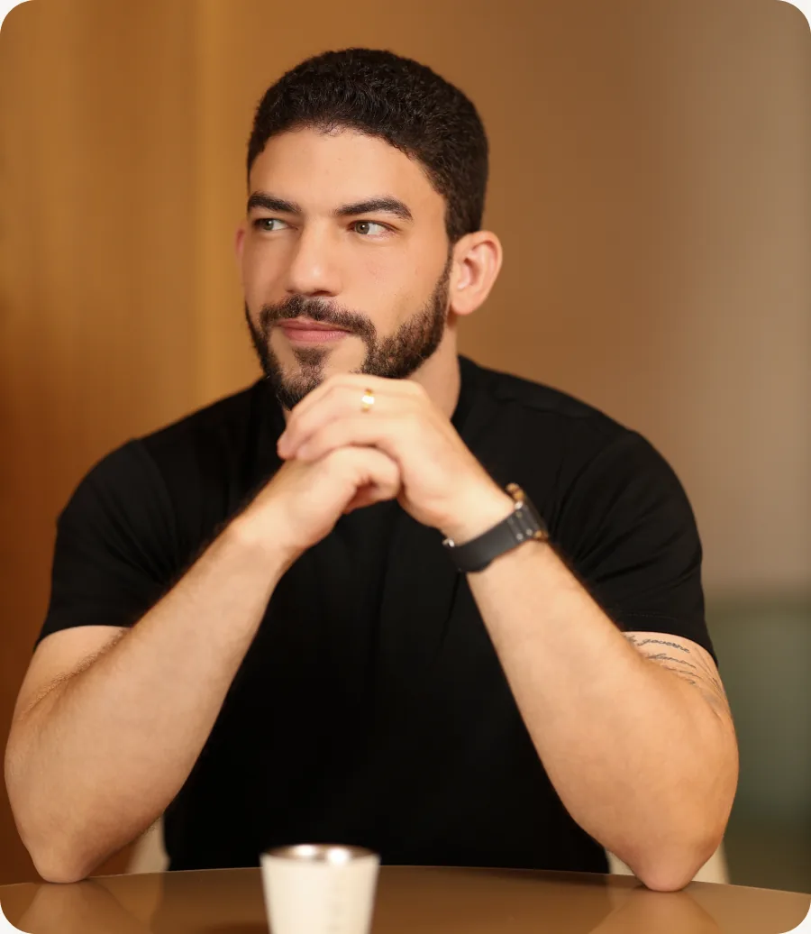 Dr. Ítalo César sentado à mesa, de camiseta preta, com as mãos entrelaçadas
