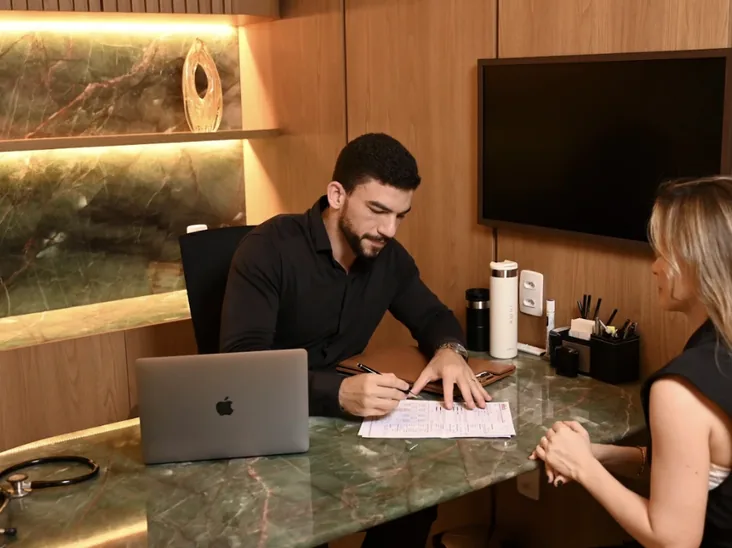 Dr. Ítalo César anotando o plano de acompanhamento durante consulta com uma paciente